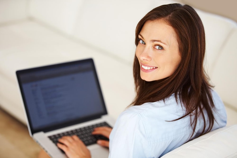 Smiling woman with a laptop on her knees.