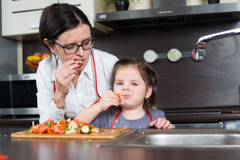 A mother eating vegetables with her daughter