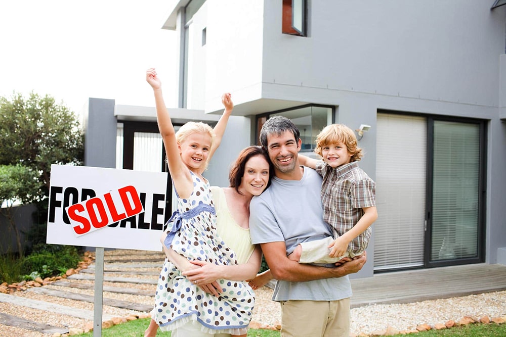 Smiling family standing in front of the sold house.