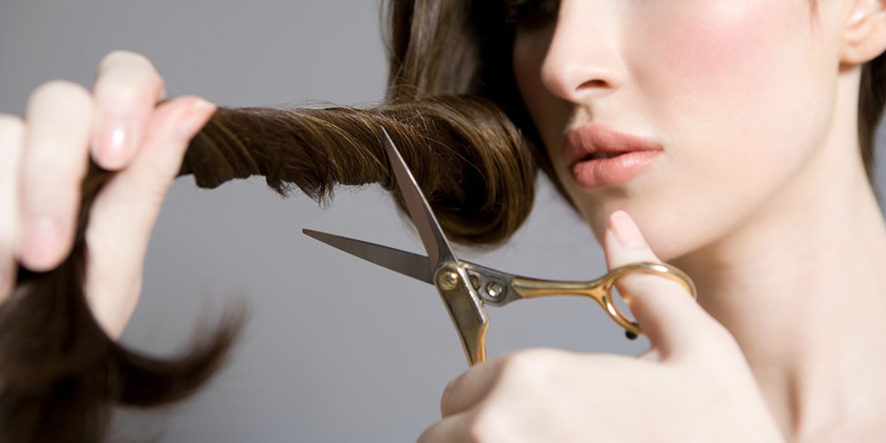 Woman holding scissors and her hair lock.