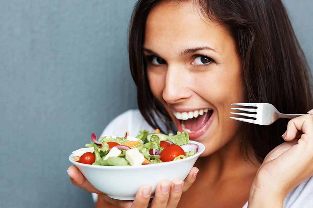 Woman holding a bowl of salad and a fork.