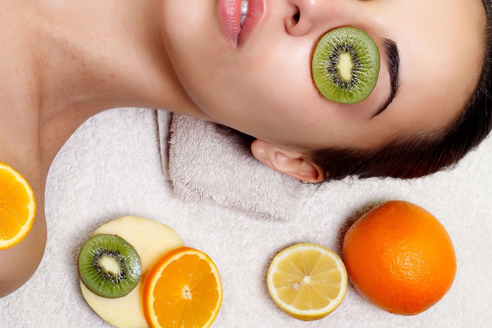 Woman with kiwi on her eye surrounded by fruits.