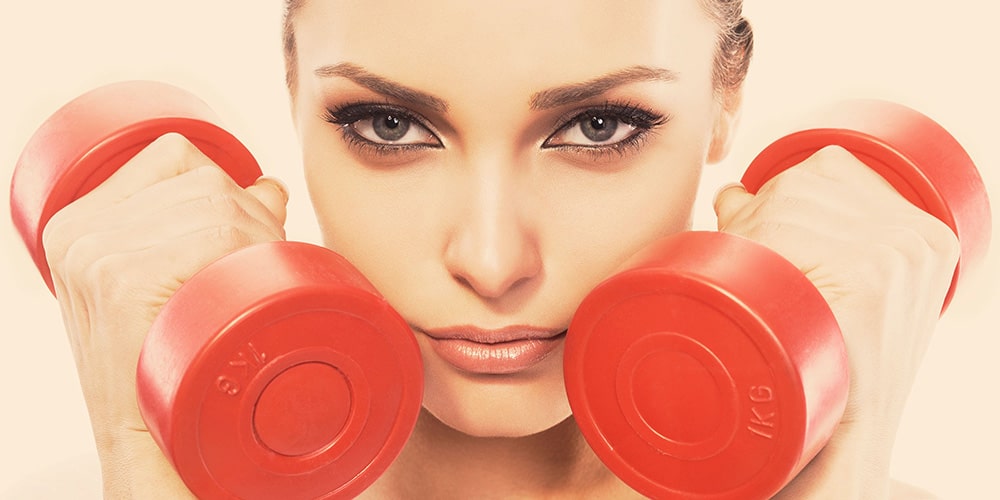 Woman holding dumbbells next to her face.