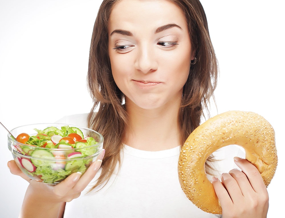 woman undecided between a donut and a plate of salad