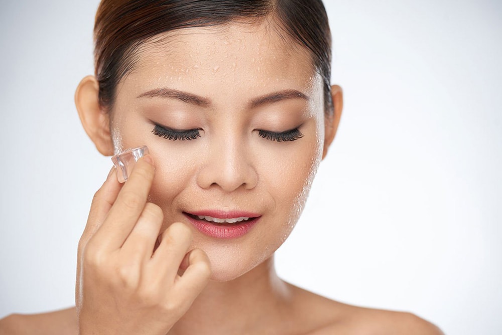 Woman applying an ice cube on her face.