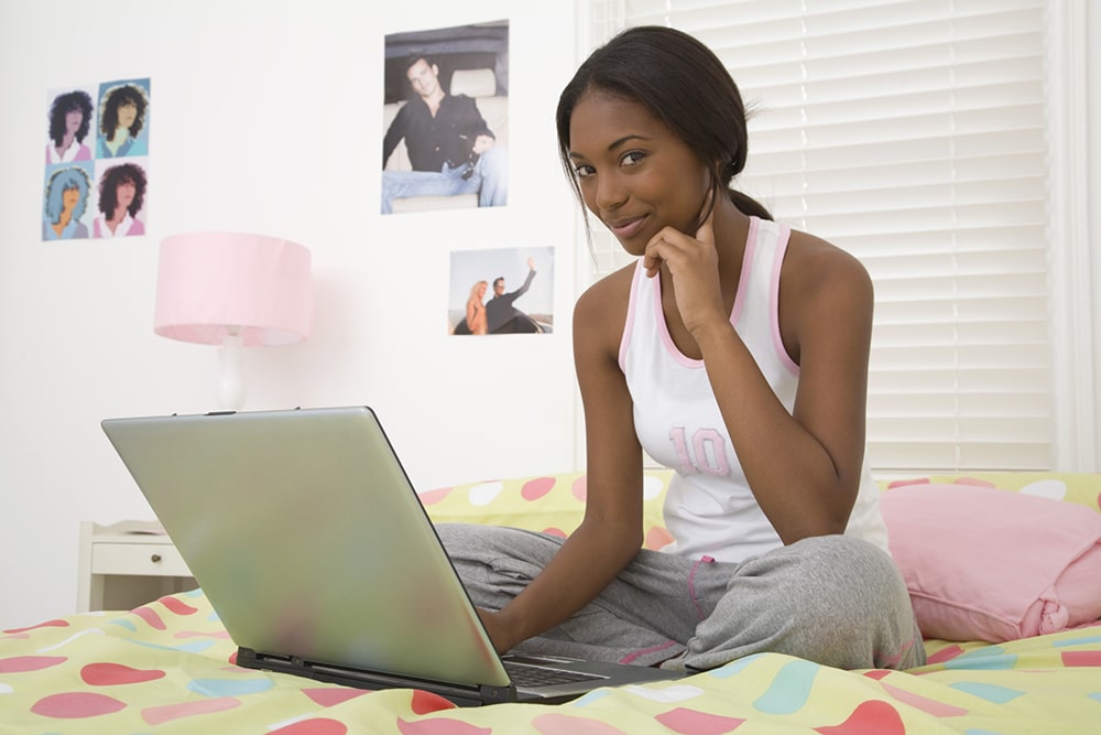 Woman sitting on the bed with a laptop.