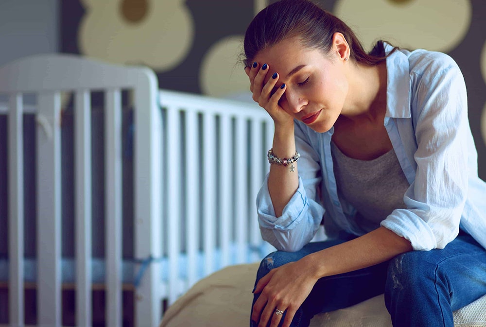 Woman sitting next to a cot bed.