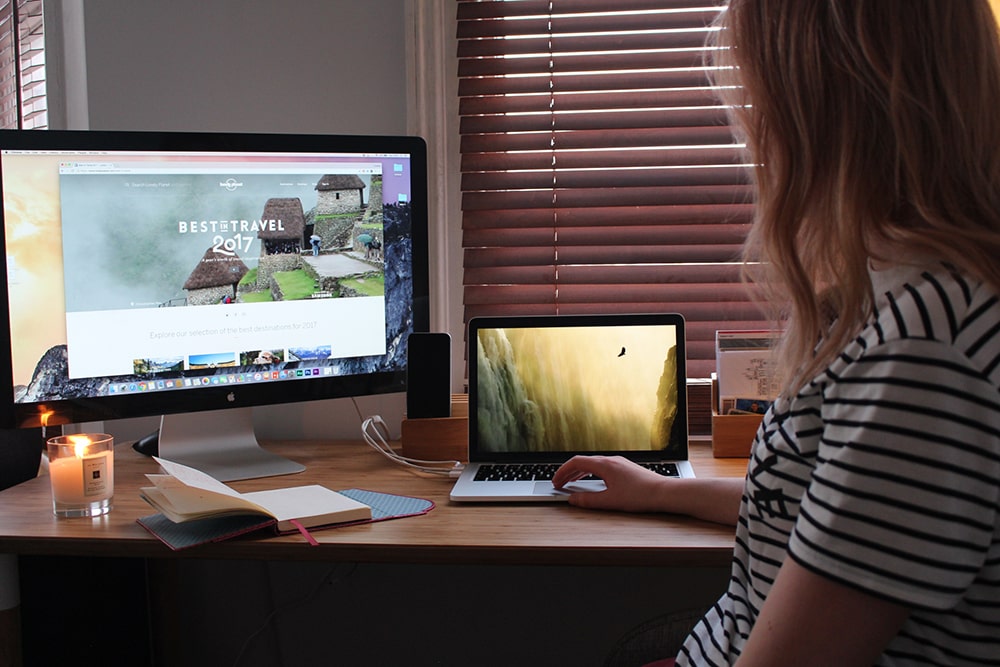 Woman sitting at the desk and watching on a laptop and a monitor.