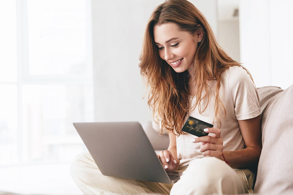 Woman working on a laptop and holding a credit card.