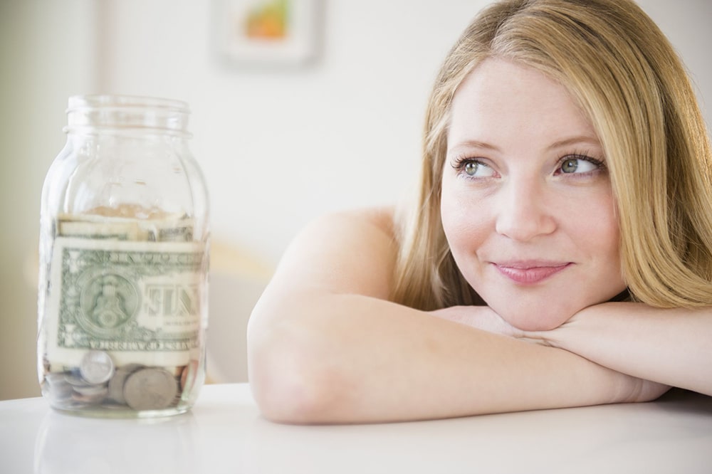 Woman looking at a jar filled with money.